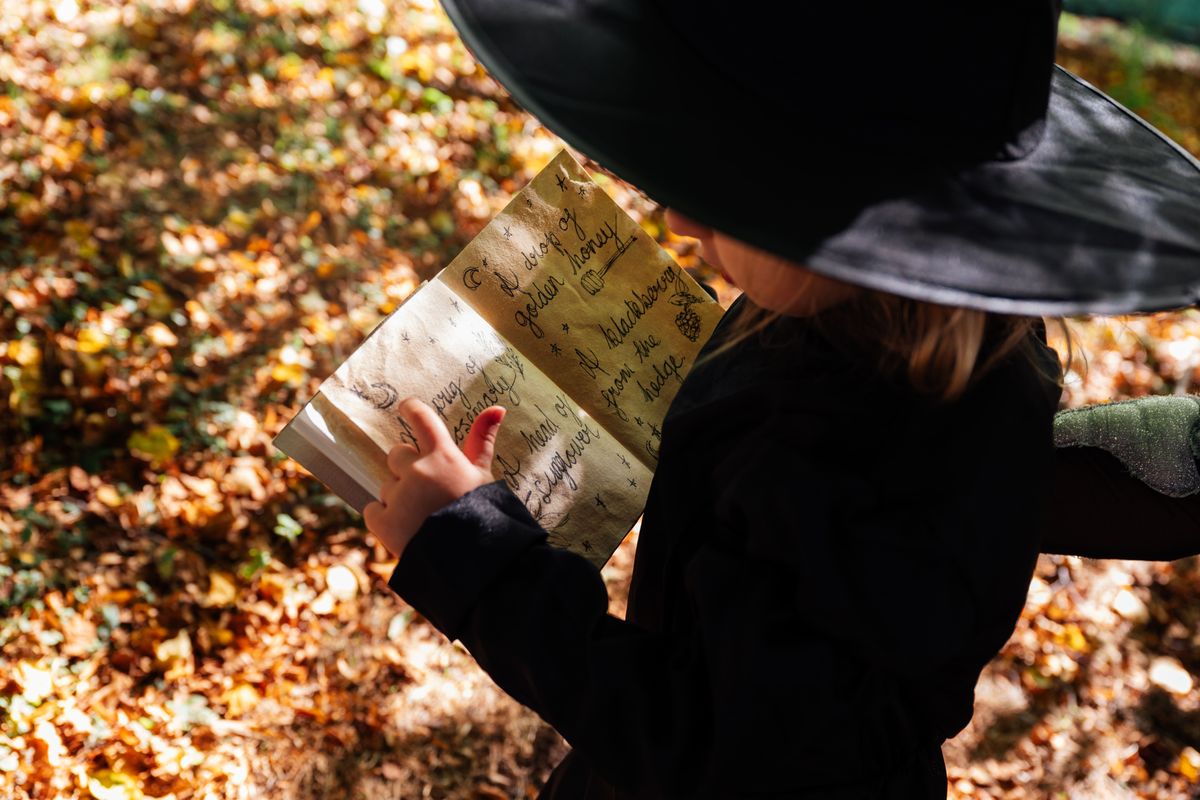 A child dressed as a witch looking at a booklet in a leafy area