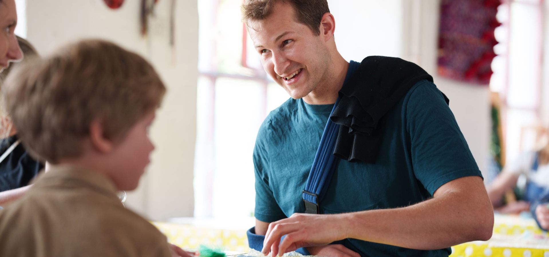 a man with a jumper over his shoulder doing a felt activity sat across from a child