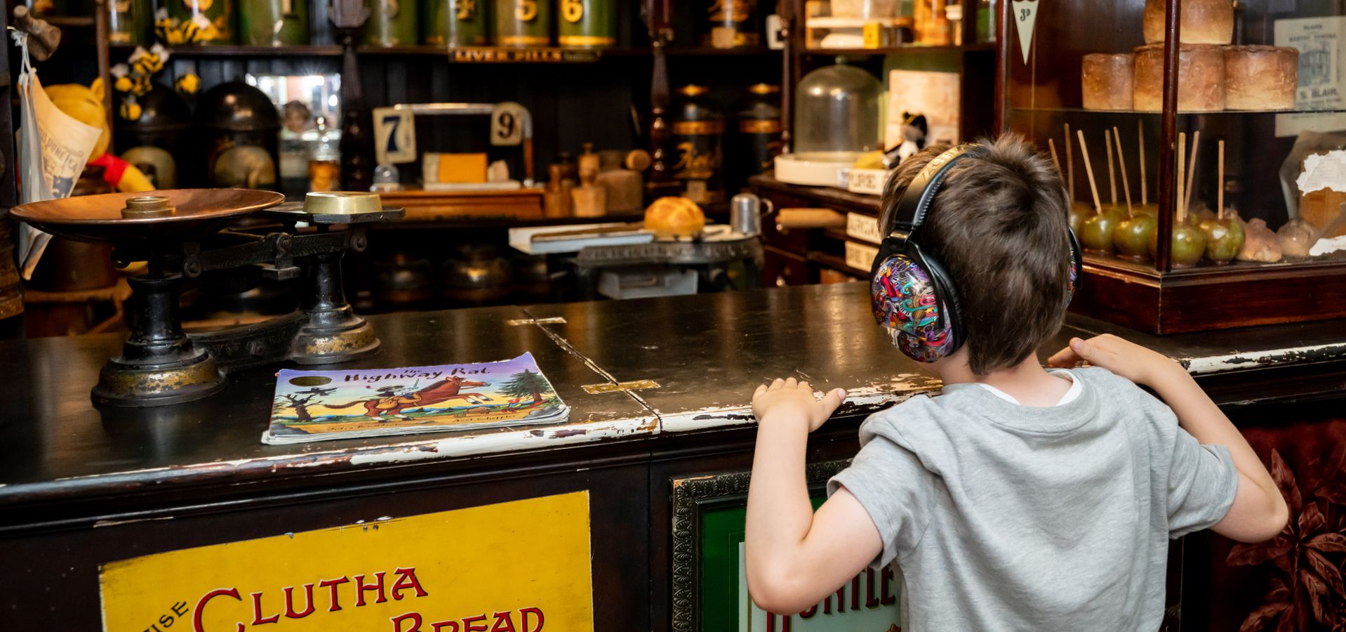 A child with ear defenders on looking over a victorian shop counter