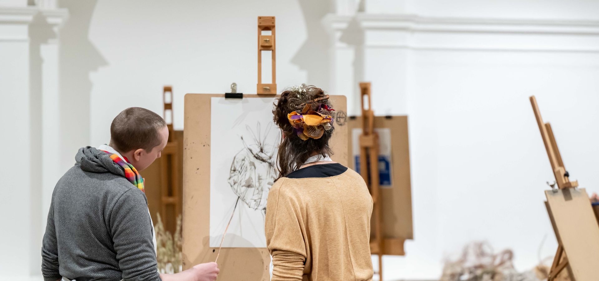 Two people working on an easel with white painting doing a stick drawing