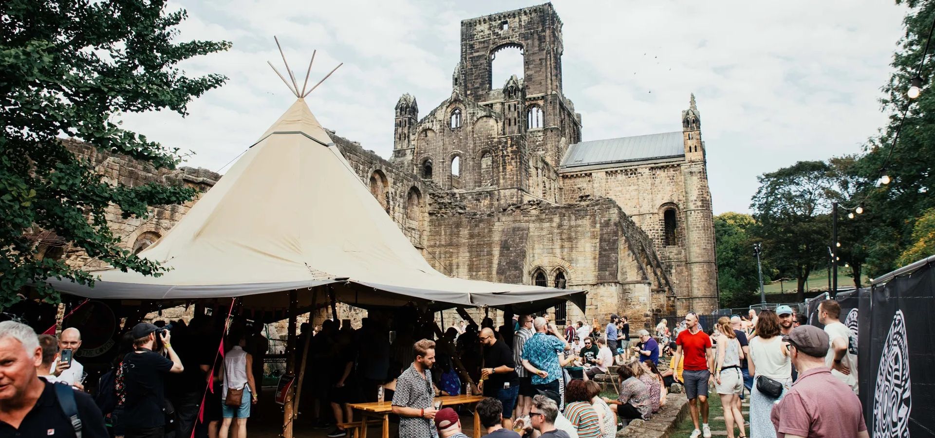 A crowd of people and a tipi in front of Kirkstall Abbey