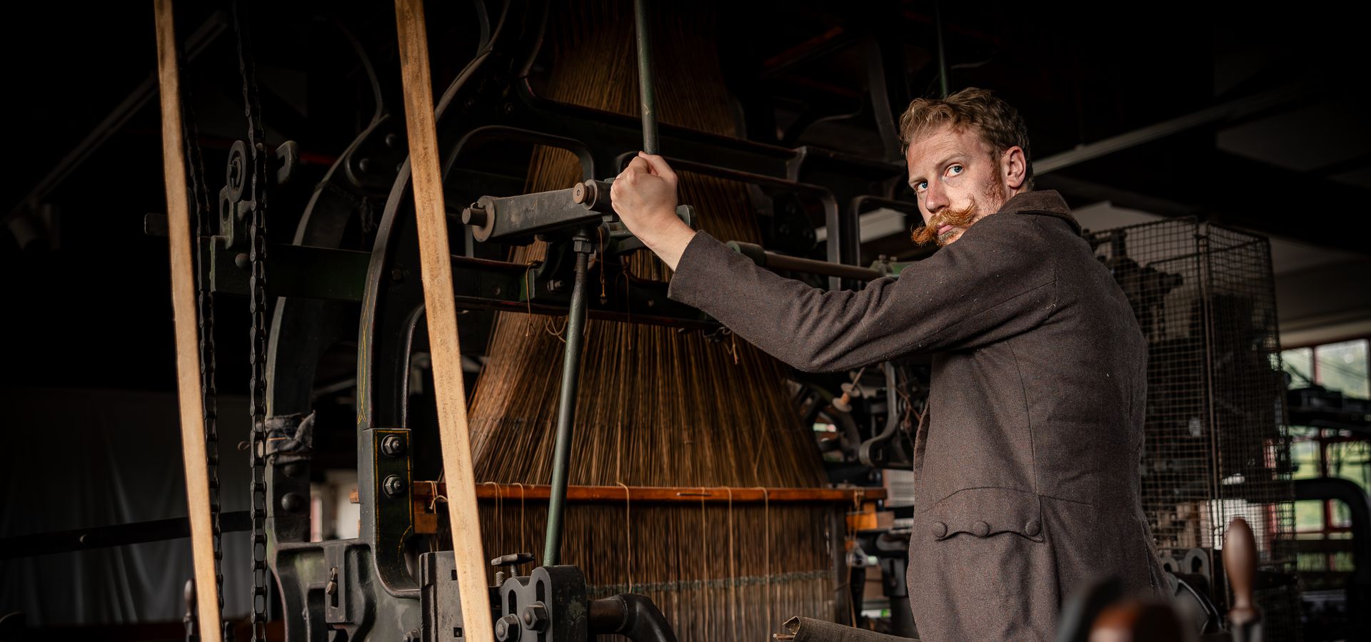 a man with a large moustache in a brown jacket using a large industrial machine in Leeds Industrial Museum