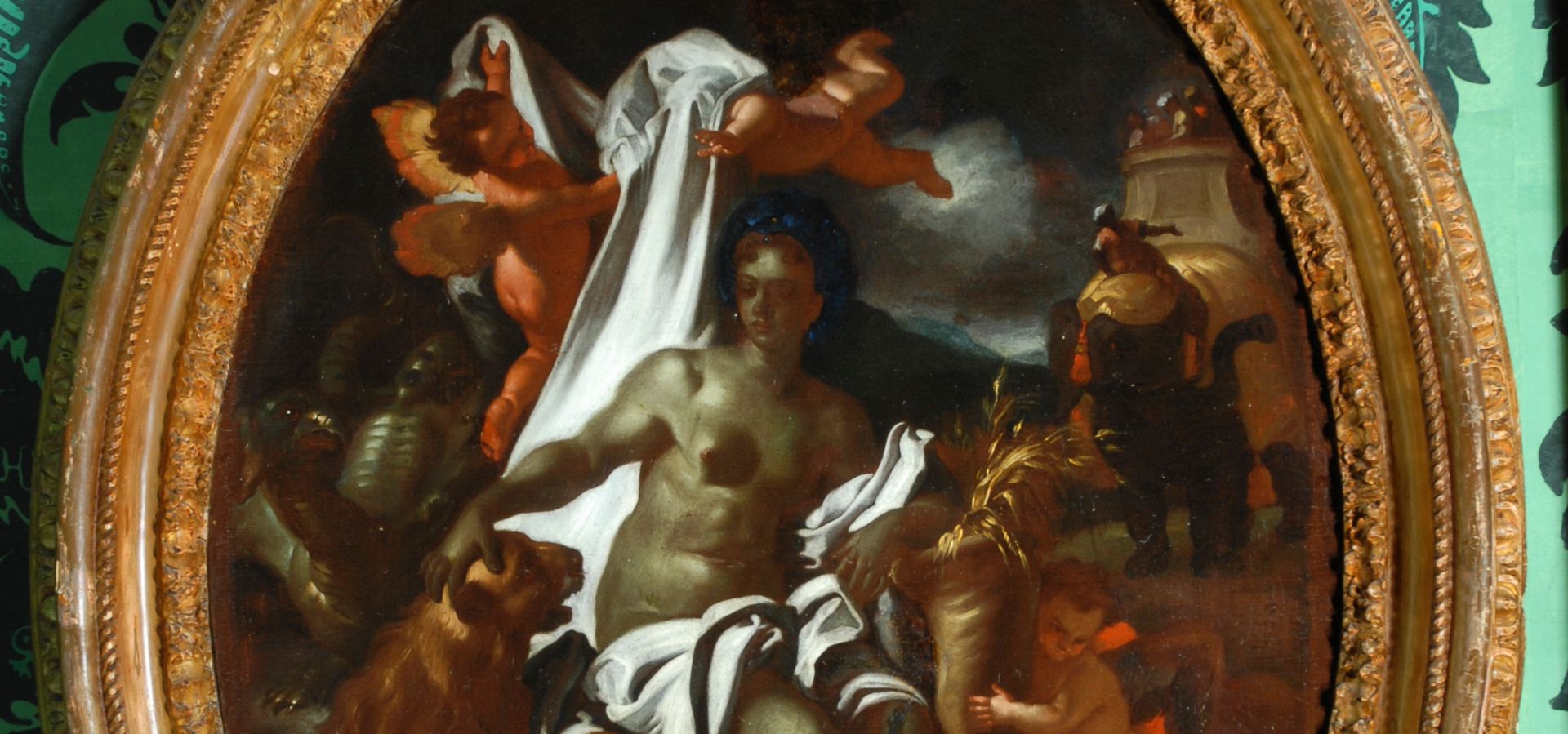 An oval frame hung on green patterned wallpaper. The frame picture is Africa by F Solimena