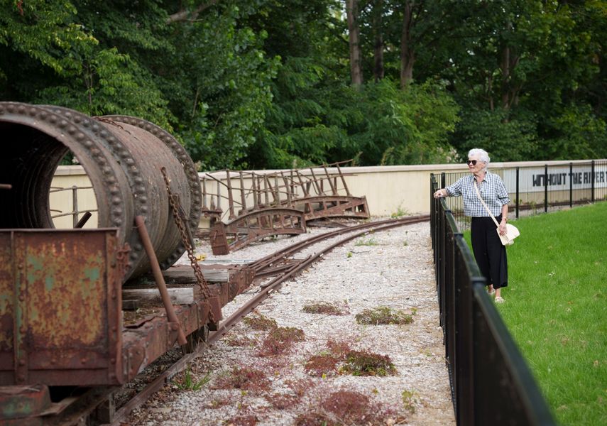 A woman stood on grass over looking a stoned area with train tracks with industrial machinery on