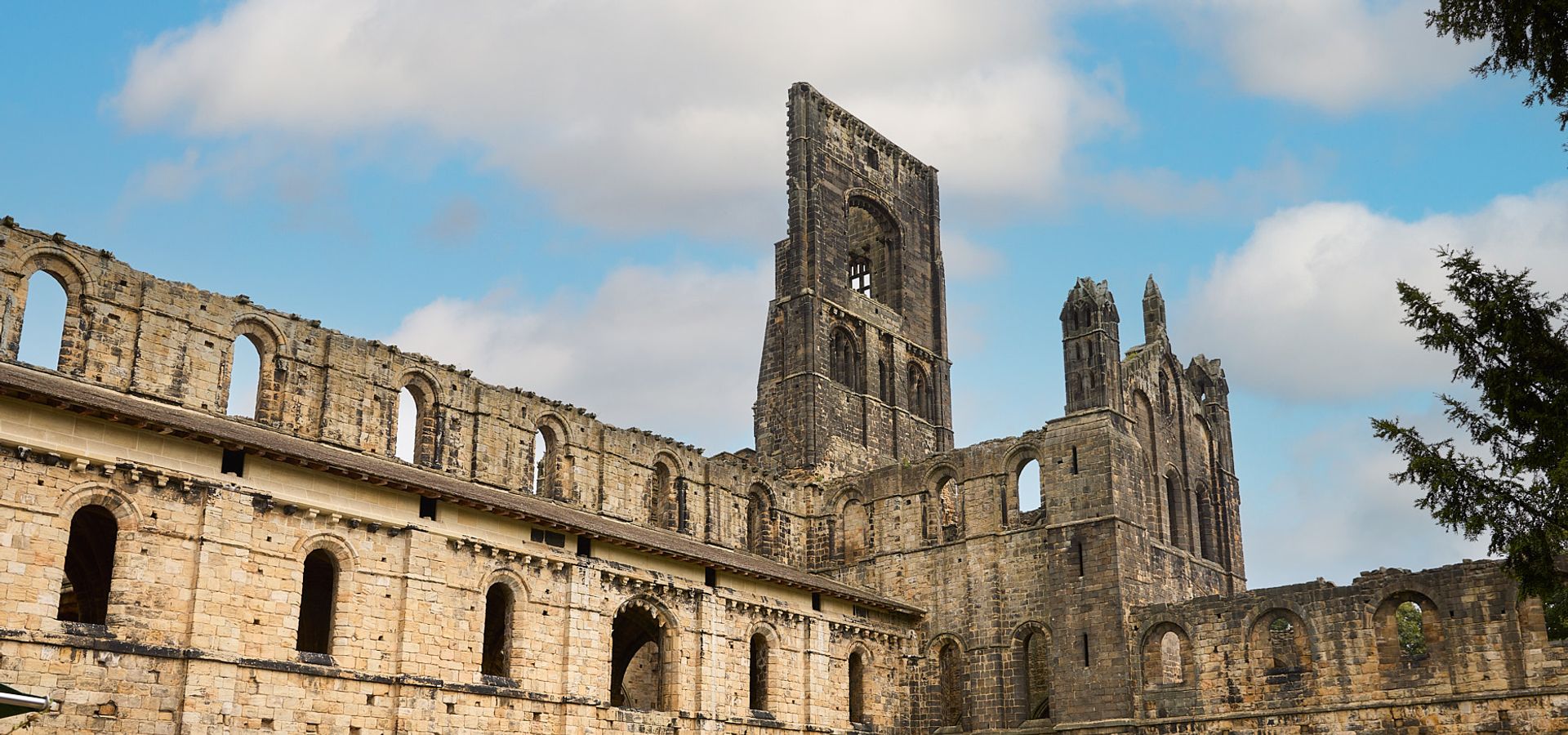 Exterior shot of Kirsktall Abbey on a sunny day with people outside.