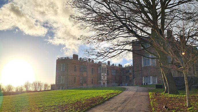 Temple Newsam House with the sun setting in the background and a path leading up to the house with a tree