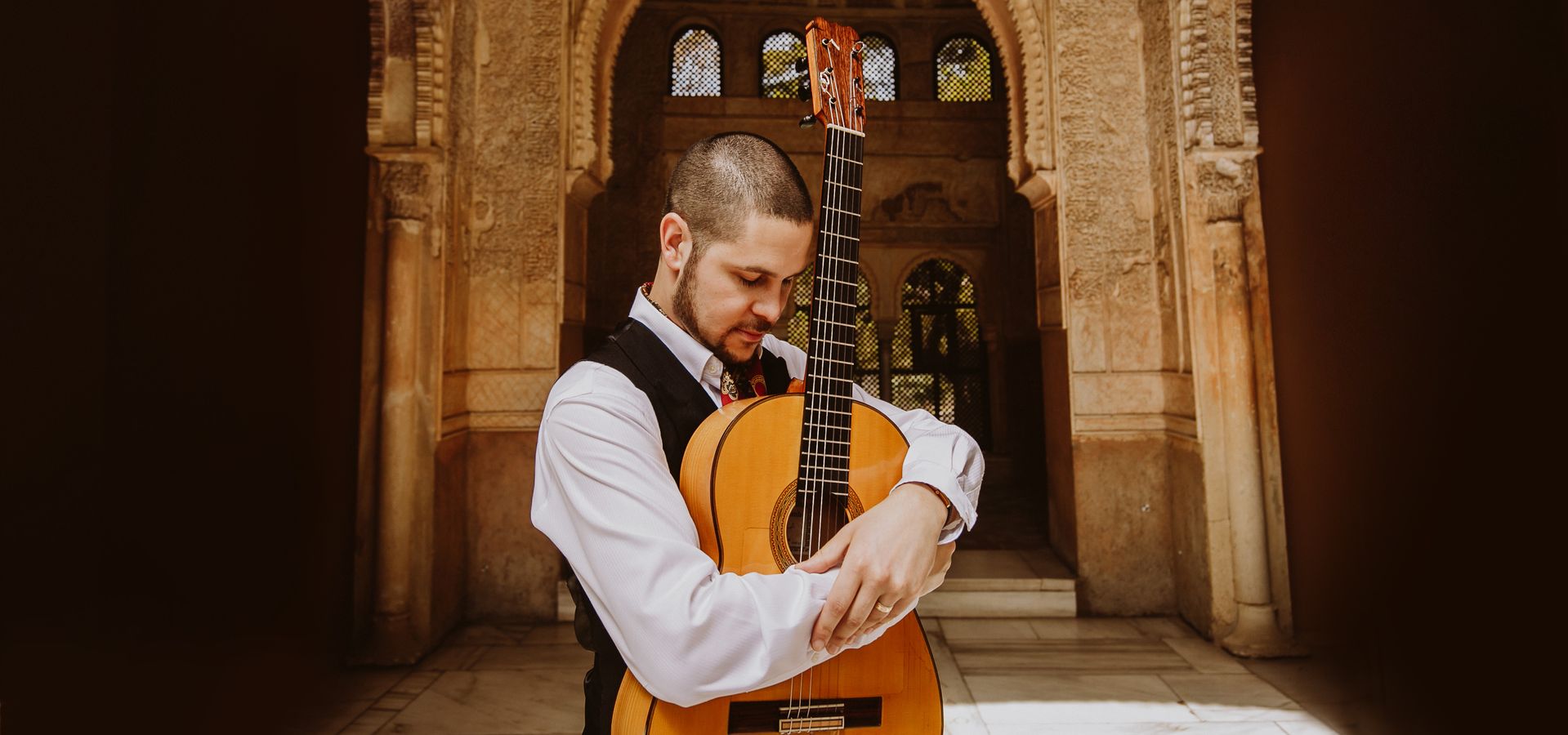 Samuel Moore stood in front of an archway with his guitar 