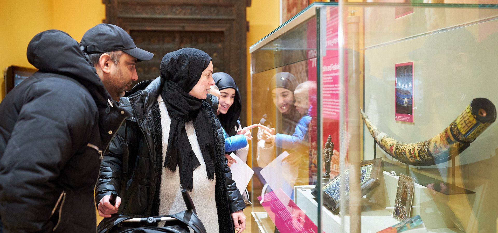 A group of adults with a pram looking into a display cabinet in the Voices of Asia exhibition