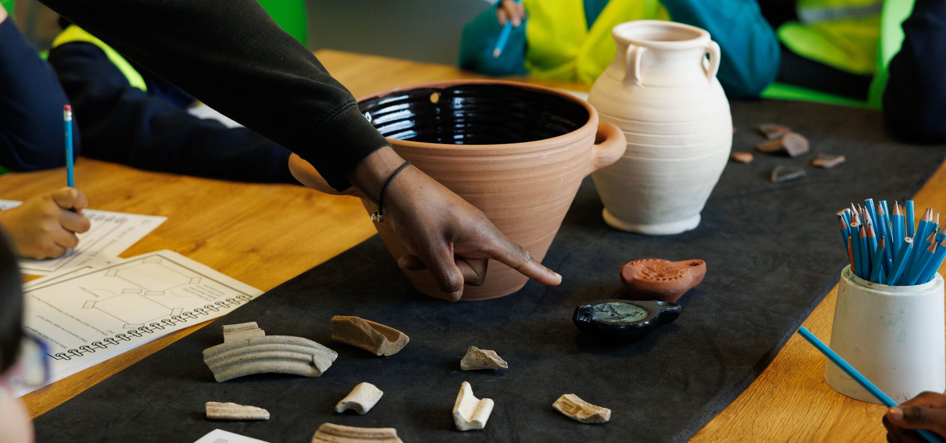 a hand pointing at pieces of pottery on a table