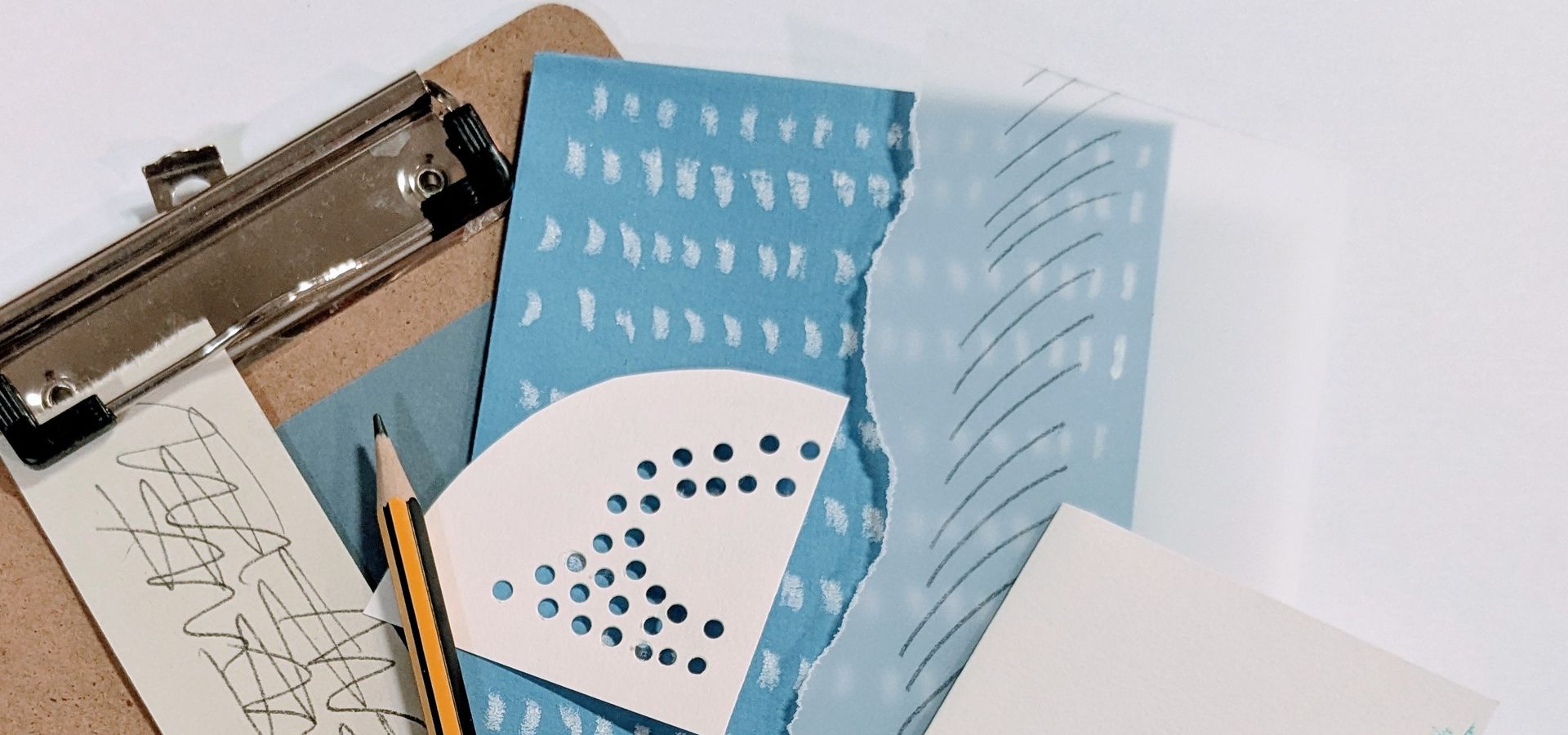A clipboard with a pile of white and blue coloured paper with cut outs and different shapes drawn on