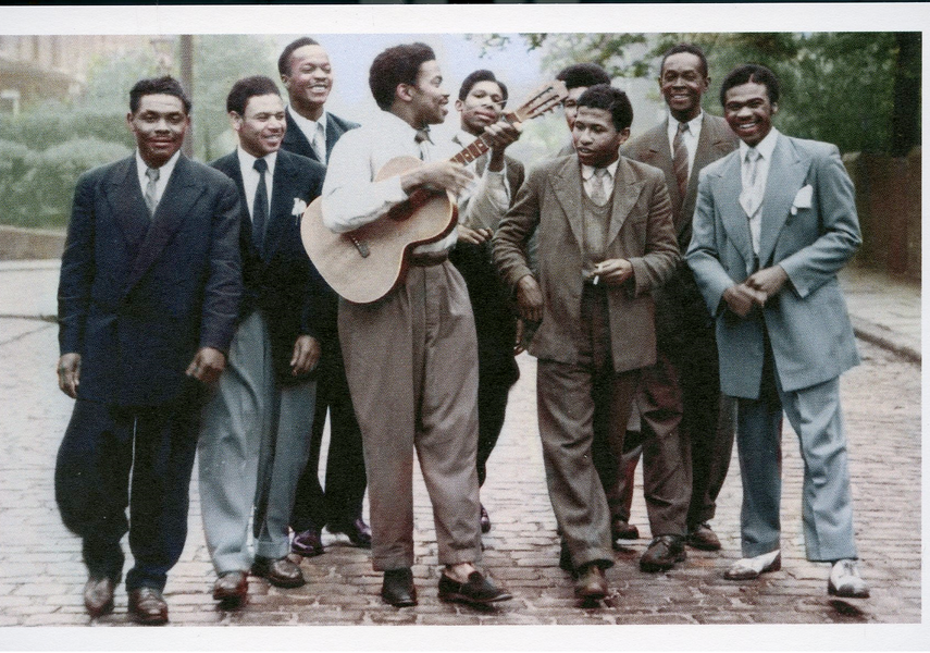 Men standing on a street in Leeds wearing suits, one is holding a guitar