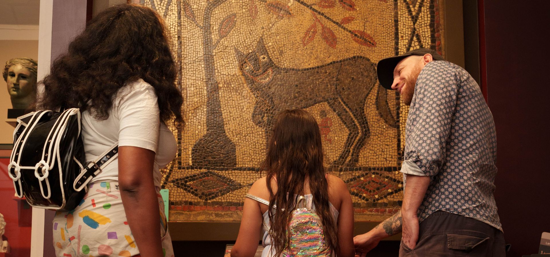 two adults with a child between them looking at a large ancient tiled wolf mural
