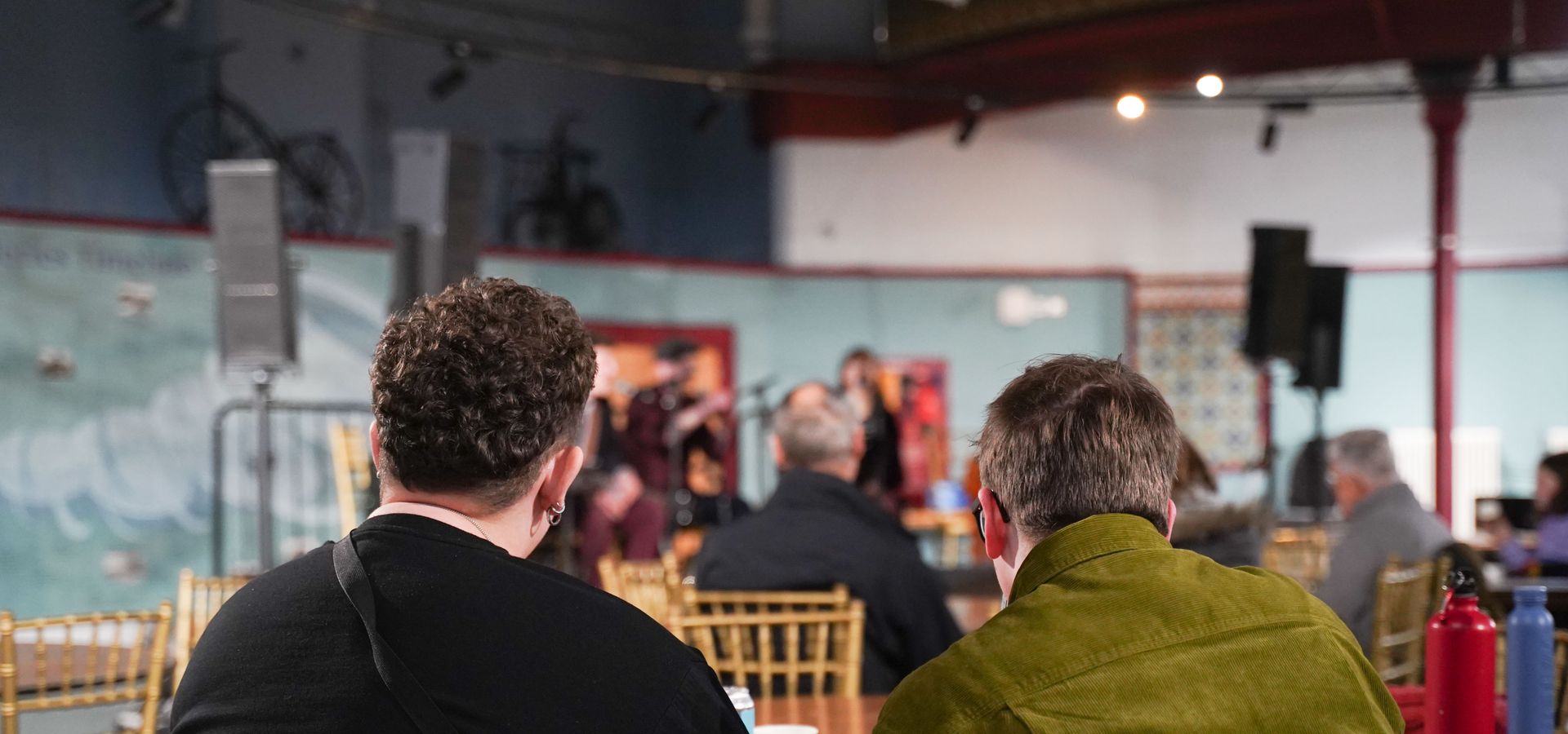 Two people sat on chairs around a table, looking at the stage in Broderick Hall