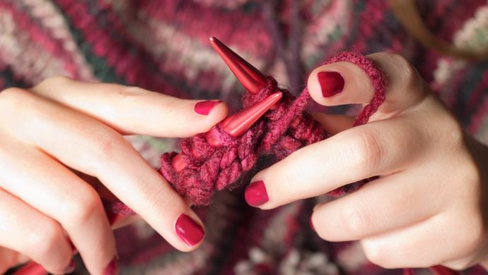 a person knitting with red wool