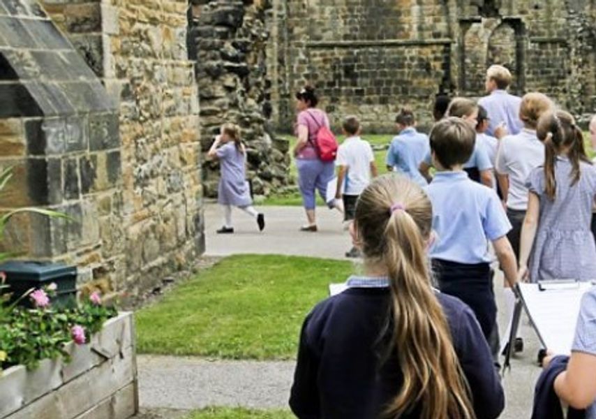 A class of children walk past a ruined abbey