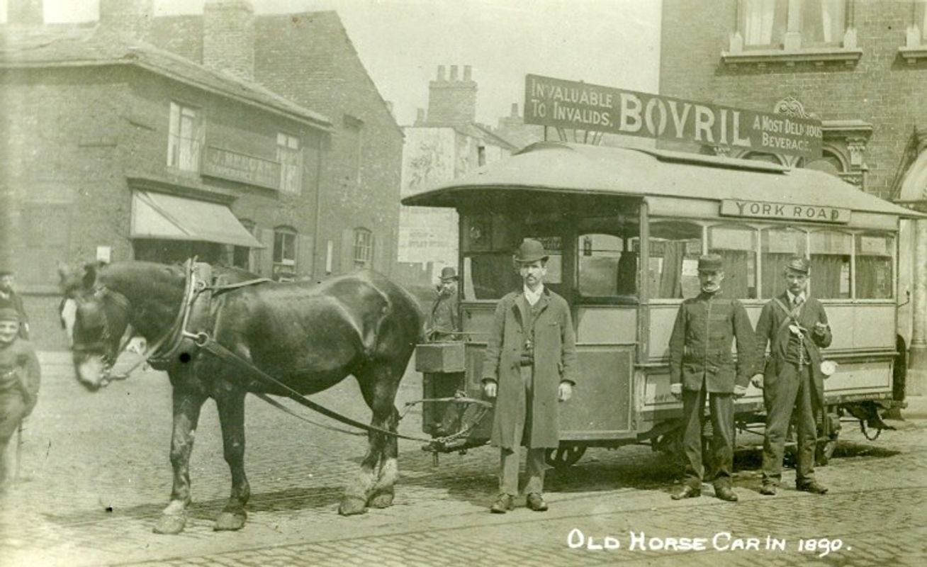 A stationary horse-drawn tram with people in front