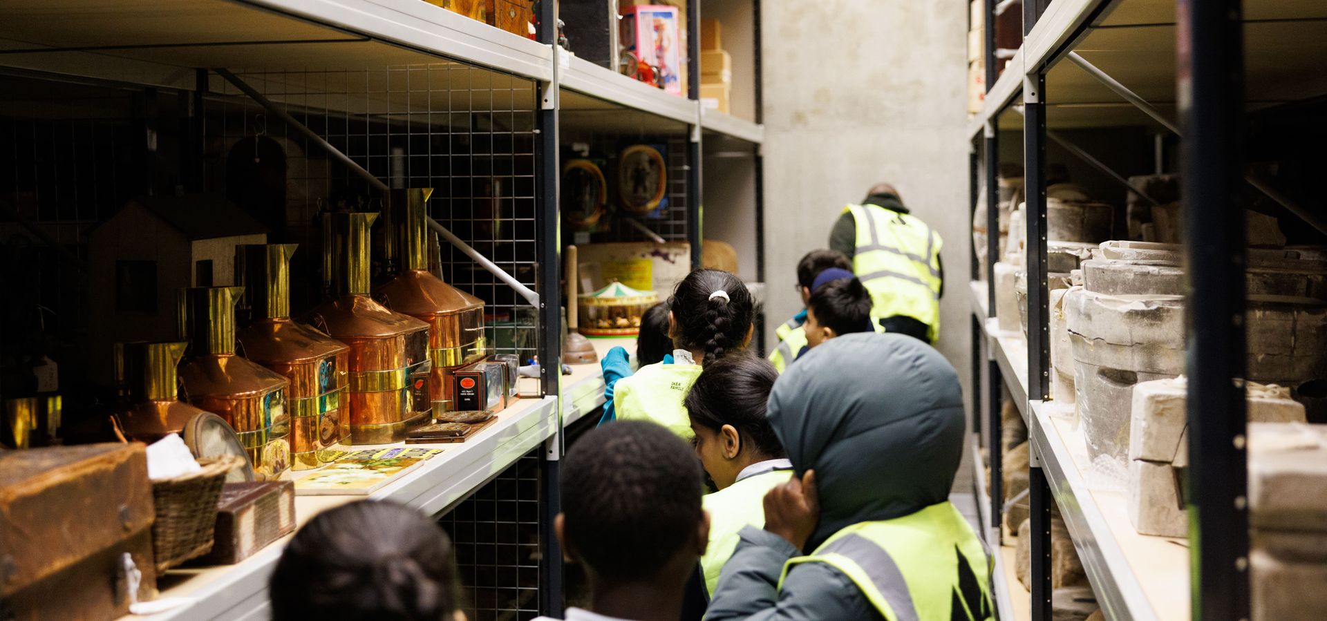 A group of children in high-vis jackets looking a shelving with collection objects on in Leeds Discovery Centre
