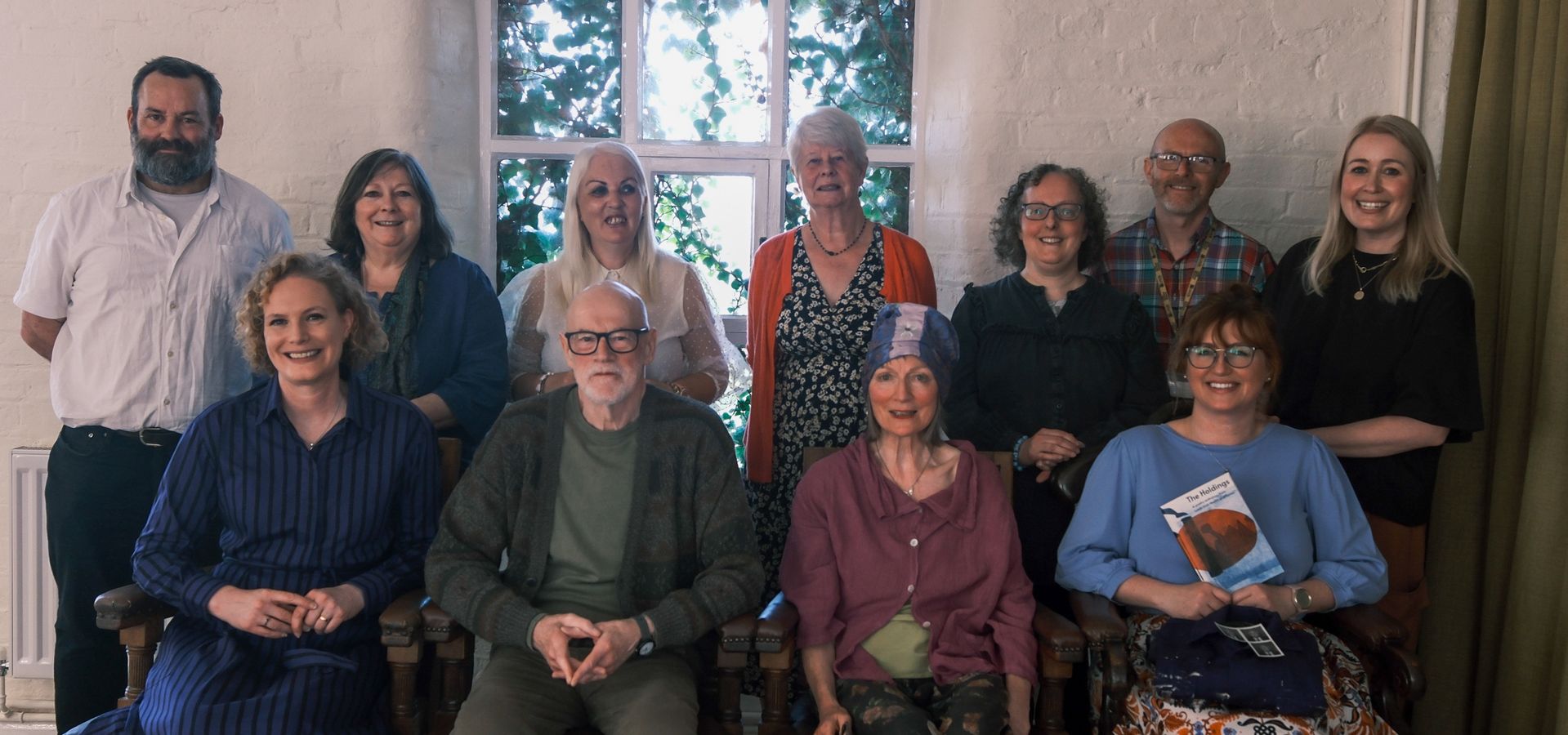 A group of 11 people smiling, one at the from holding the poetry anthology