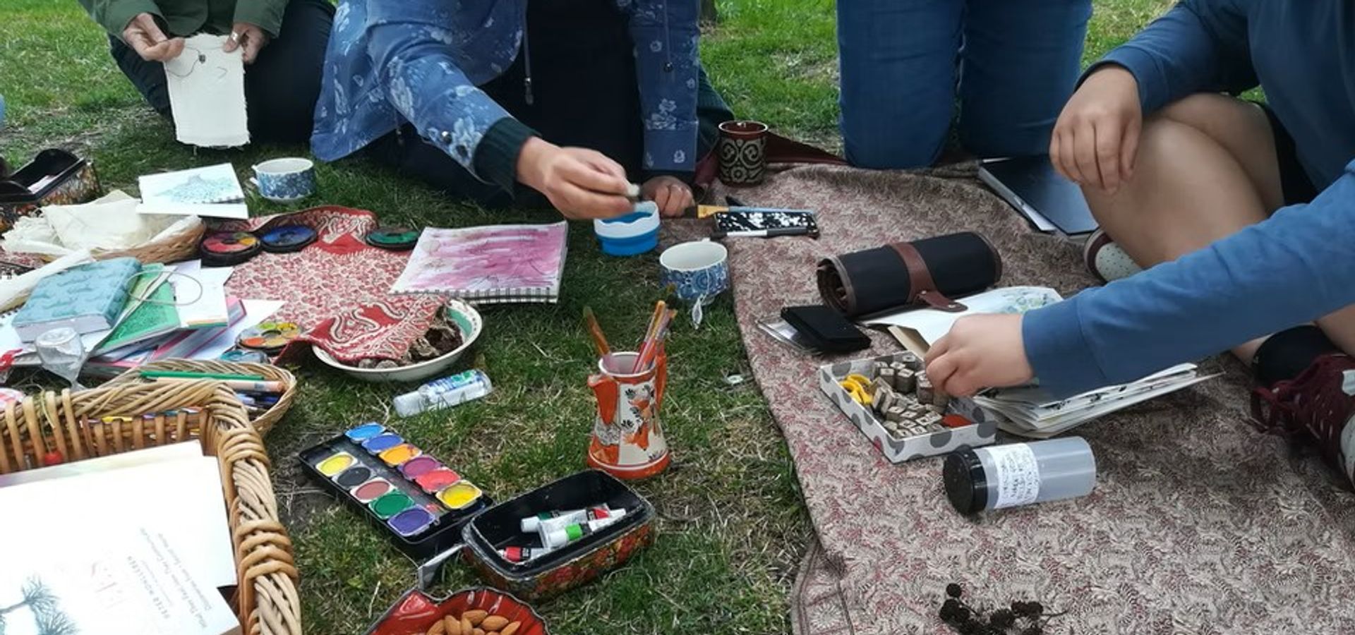 A blanket on grass with people painting watercolours in booklets