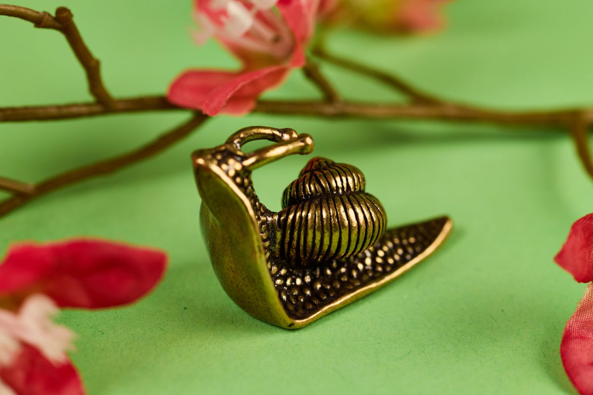 A close up of a brass snail with a green background and petals behind