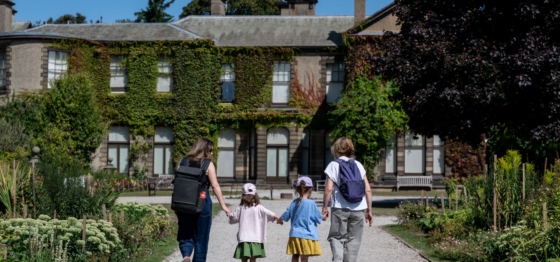 Two adults and 2 children holding hands walking up a pathway to Lotherton Hall