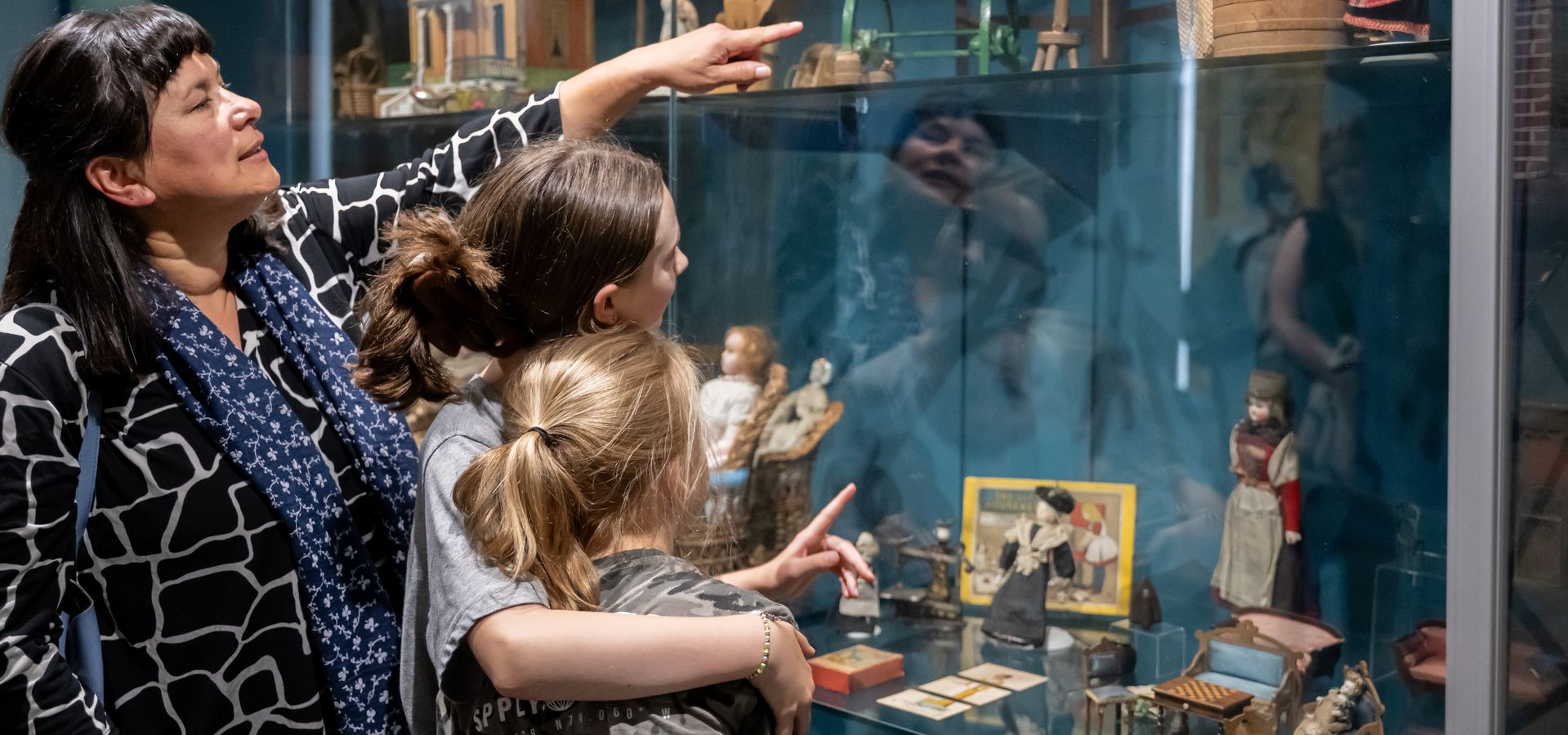 A woman and 2 children looking at glass cases 