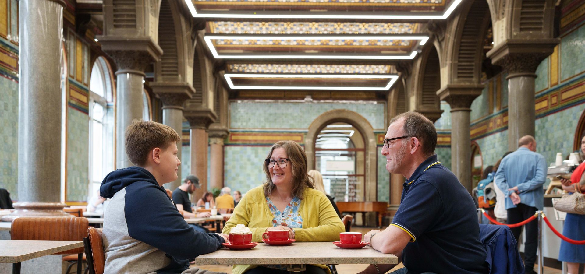 2 adults and a child sat at a table in a cafe with coffee