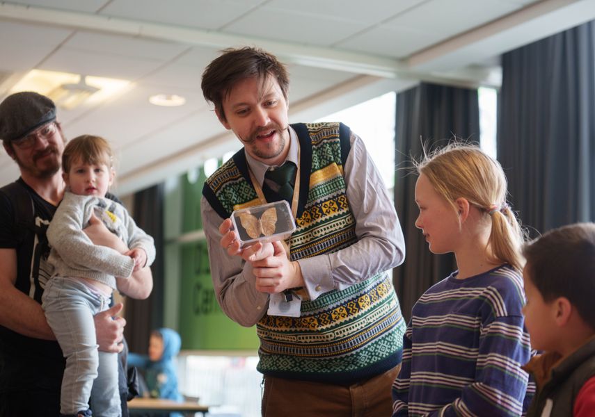 A learning assistant holding a boxed moth to a group of children