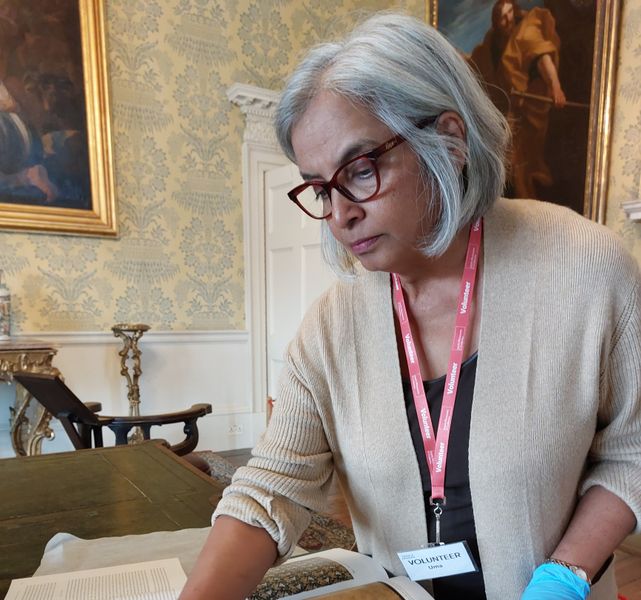 A volunteer wearing blue gloves looking at books and fabrics at Temple Newsam house