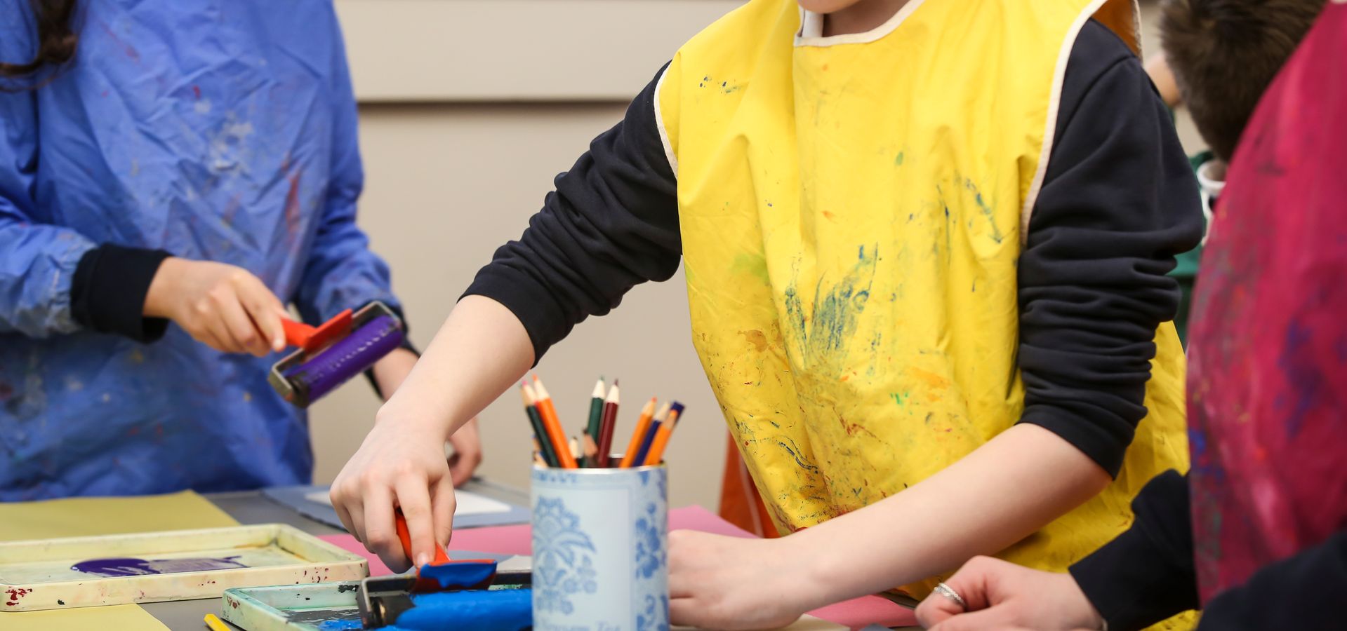 Children wearing aprons using printing rollers to create art