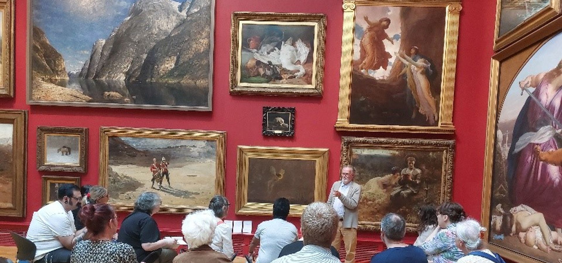 A group of people listening to a talk infront of a wall with artwork