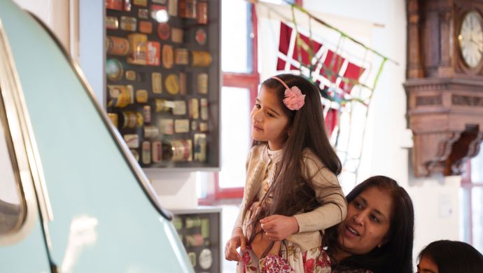 An adult lifting up a child to look at a car in the museum