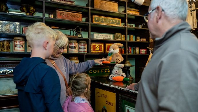 Two adults and 2 children looking at an old fashioned shop counter with rabbits on