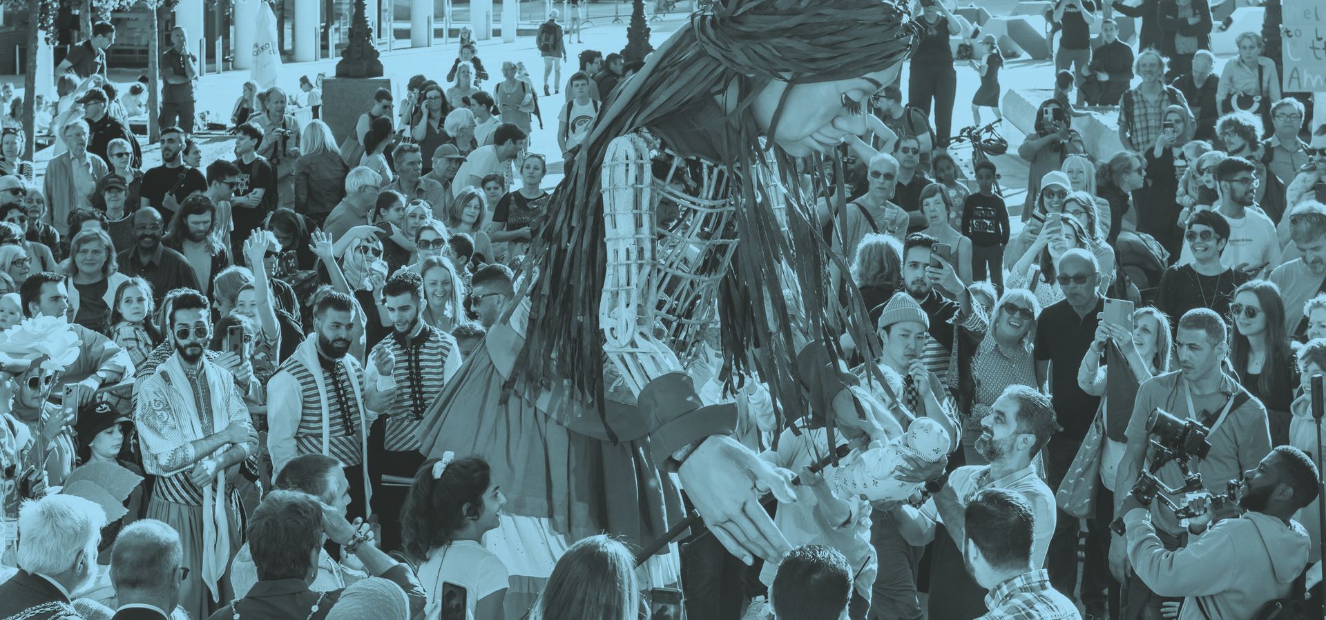 A black and blue image of a crowd looking at a large puppetter