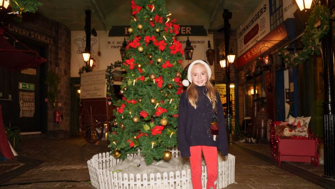 A child with a Mr Claus Christmas has on stood in front of the tree