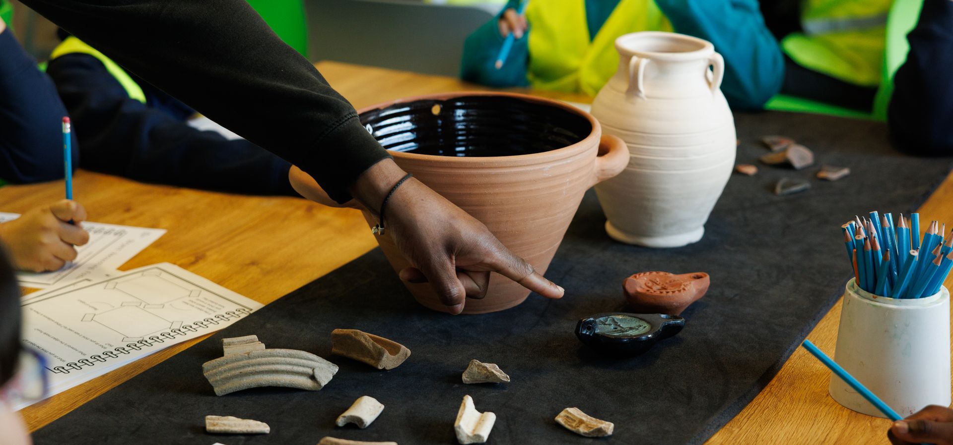 A group of children pointing and looking at museum objects on a table