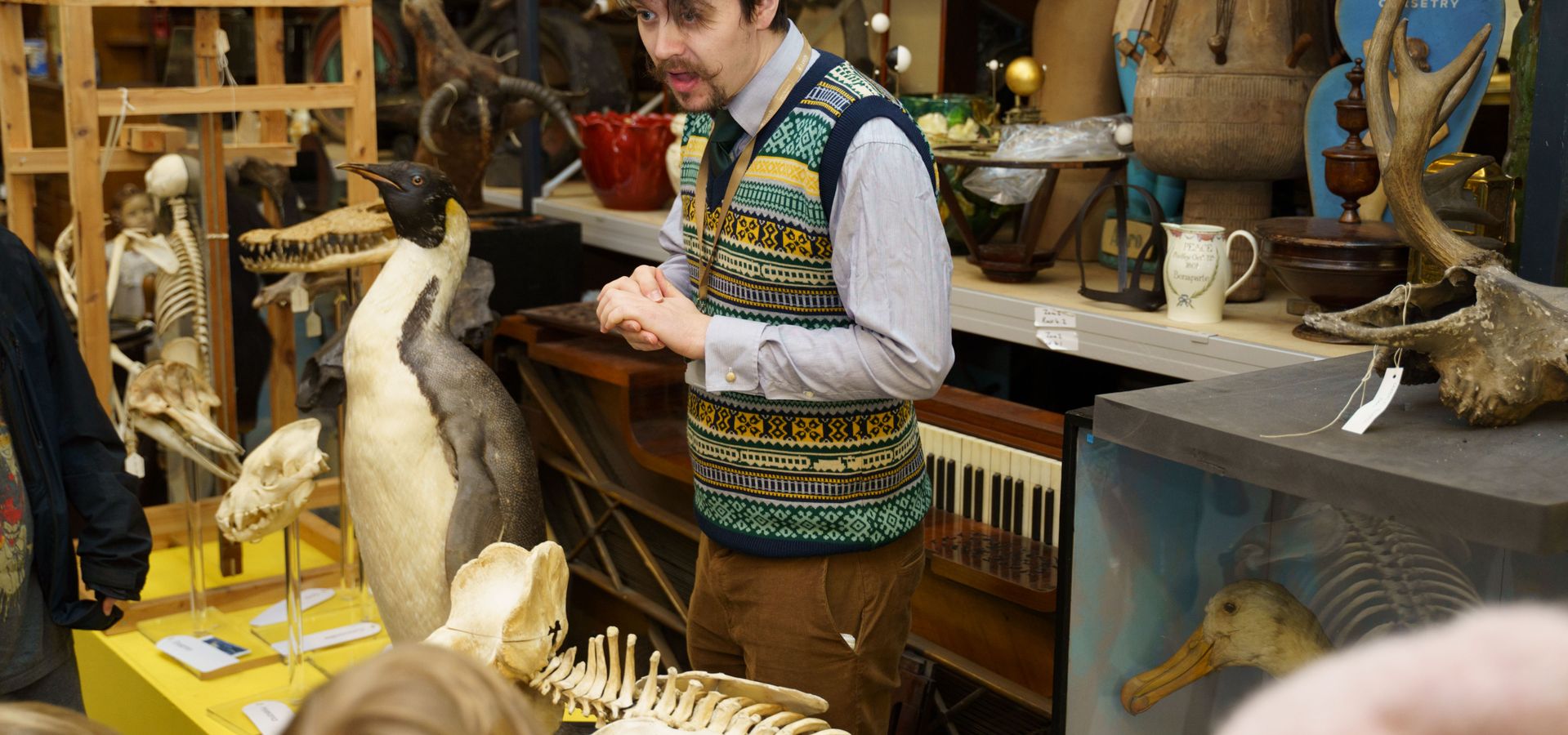 A tour guide stood next to a taxidermy penguin and objects from the collection store