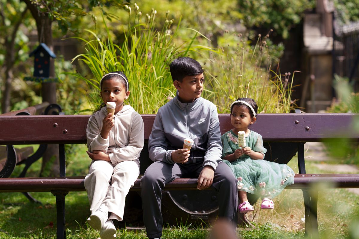3 children sat on a bench in a garden eating ice creams