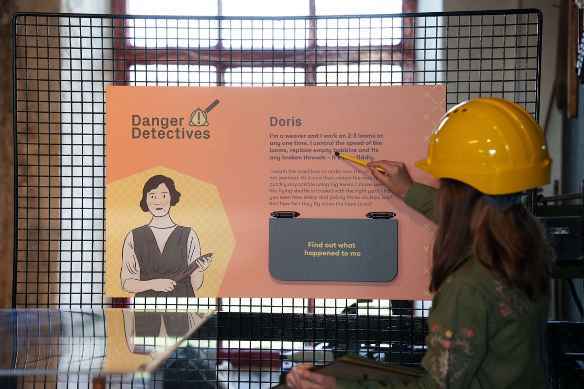 A child in a yellow hard hat point at Danger Detective boards learning about Doris