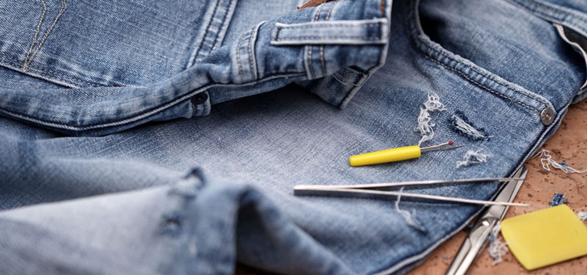 A pair of ripped denim jeans undergo repair.