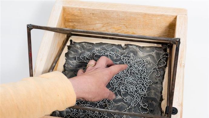 A hand reaching into a wooden box feeling an object