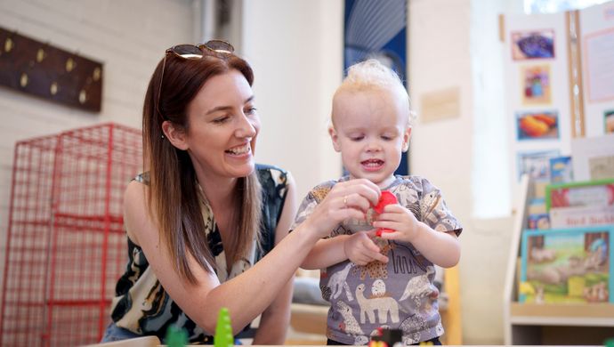 a toddler and adult playing with a toy train track