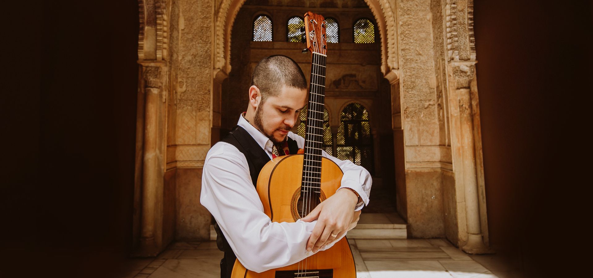 Samuel Moore stood in front of an archway with his guitar 