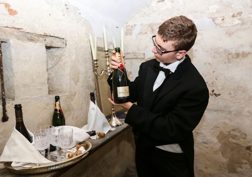 A child dressed as a butler holding champange in a cellar