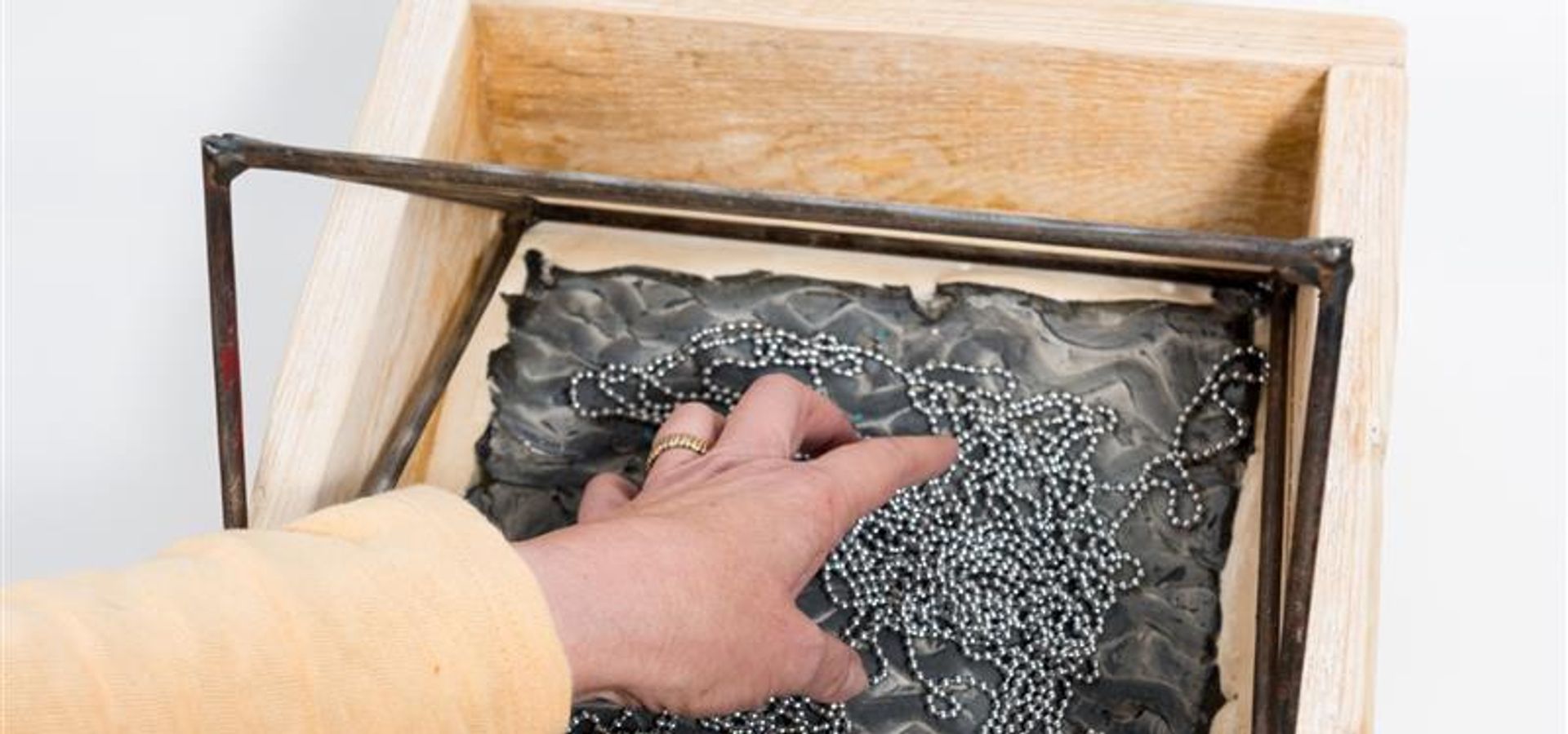 A hand reaching into a wooden box feeling an object