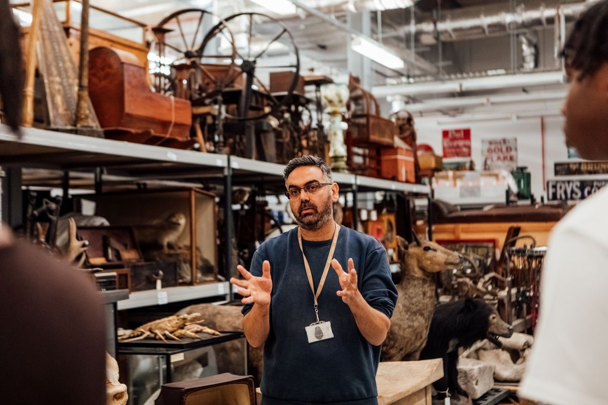 A curator giving a talk in front of shelves of objects