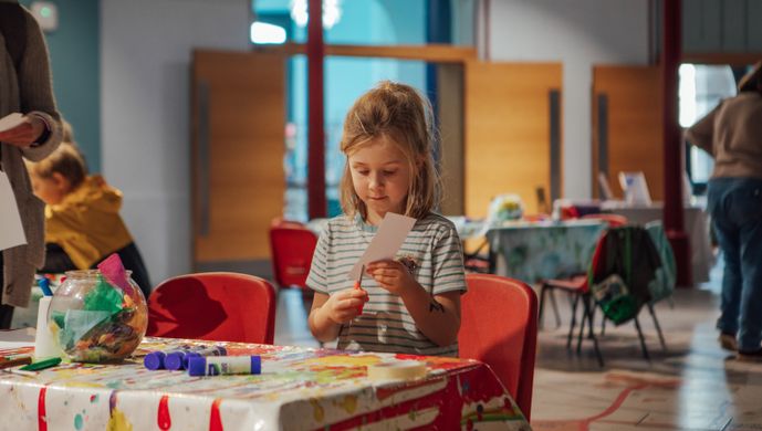 Girl at arts and crafts table, cutting paper.