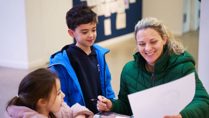 An adult and 2 children looking at drawing whilst sat at a table