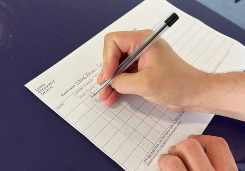 Someone filling in a visitor information sheet at Leeds Discovery Centre