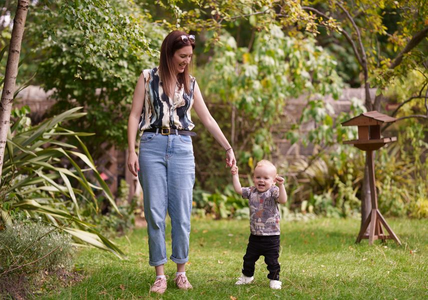 A woman holding a toddlers hand whilst walking in a garden